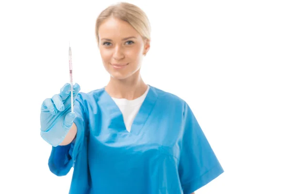 Усміхнена молода медсестра тримає шприц для ін'єкцій і дивиться на камеру ізольовано на білому — стокове фото