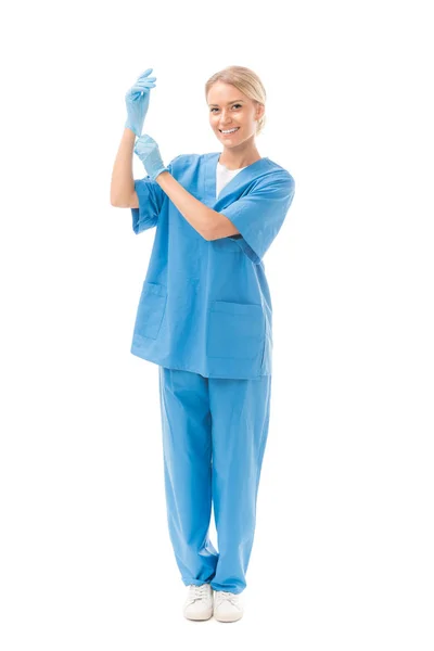 Joven enfermera sonriente poniéndose guantes de goma aislados en blanco - foto de stock