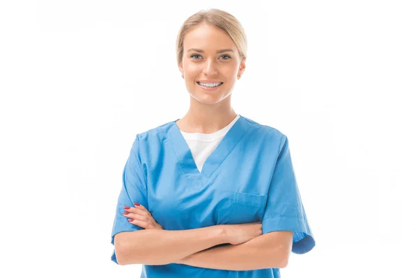 Усміхнена молода медсестра з схрещеними руками дивиться на камеру ізольовано на білому — стокове фото