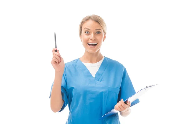 Expressive young nurse with creative idea holding clipboard and pointing up isolated on white — Stock Photo