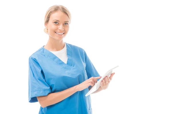 Glückliche junge Krankenschwester arbeitet mit digitalem Tablet und schaut auf Kamera isoliert auf weiß — Stockfoto