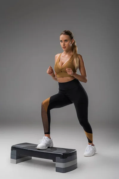 Sportive young woman working out on step aerobics board on grey — Stock Photo