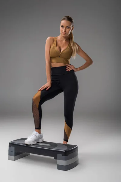 Sportliche junge Frau mit Aerobic-Trittbrett auf grau — Stockfoto