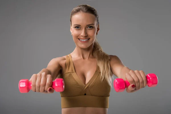 Nahaufnahme Porträt einer sportlich glücklichen jungen Frau beim Training mit Hanteln auf grau — Stockfoto