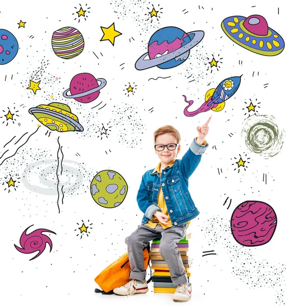 Smiling schoolboy pointing up while sitting on pile of books with backpack, isolated on white with fantasy universe, planets and spaceships — Stock Photo