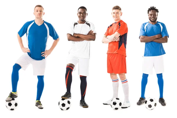 Confiados jóvenes futbolistas multiétnicos de pie con bolas y mirando a la cámara aislada en blanco - foto de stock