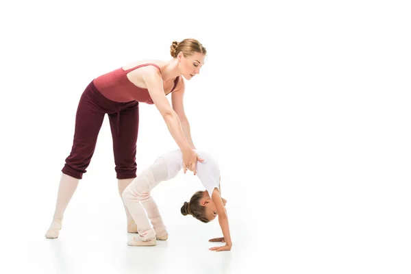 Female trainer holding little kid while she doing gymnastics bridge isolated on white background — Stock Photo