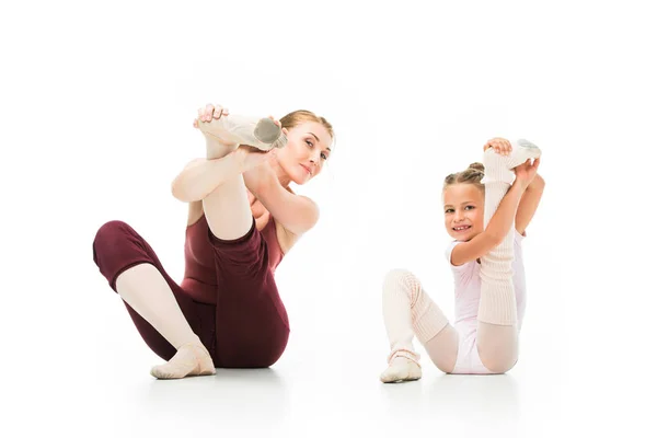 Pequena bailarina feliz e seu treinador feminino esticando as pernas isoladas no fundo branco — Fotografia de Stock