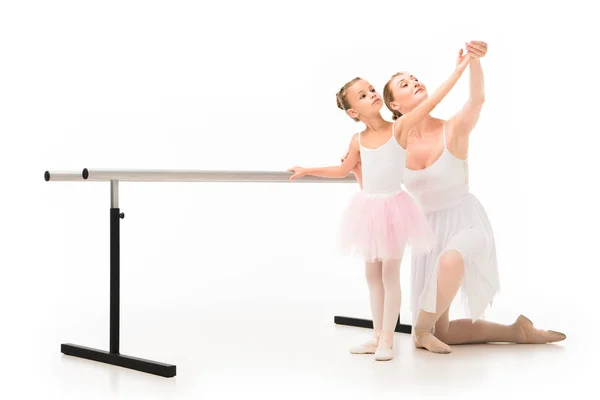 Happy female teacher in tutu helping little ballerina exercising at ballet barre stand isolated on white background — Stock Photo