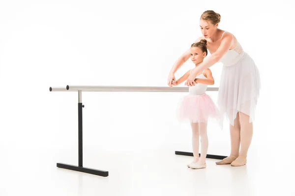 Enseignante en tutu aidant petite ballerine pratiquant au stand de barre de ballet isolé sur fond blanc — Photo de stock