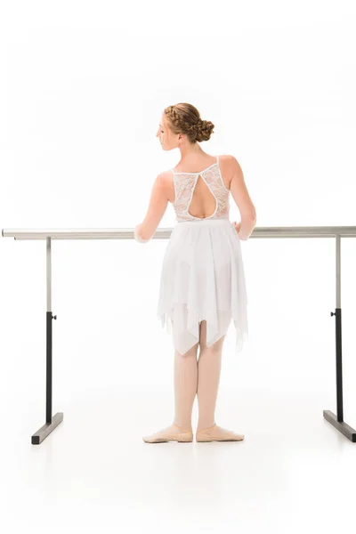 Vue arrière de l'élégante ballerine en tutu et pointes pratiquant au pied de la barre de ballet isolé sur fond blanc — Photo de stock
