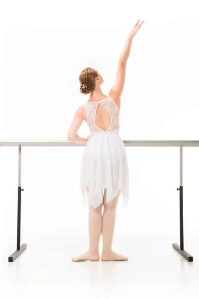 Vue arrière de la ballerine en tutu et chaussures de pointe s'exerçant au pied de la barre de ballet isolé sur fond blanc — Photo de stock