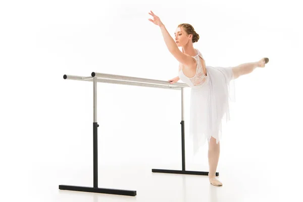 Adult ballerina in tutu and pointe shoes exercising at ballet barre stand isolated on white background — Stock Photo