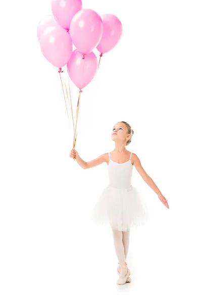 Adorable pequeña bailarina en tutú mirando hacia arriba mientras baila con globos rosados aislados sobre fondo blanco - foto de stock
