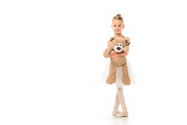 Улыбающаяся маленькая балерина в пачке, стоящая с плюшевым мишкой на белом фоне — стоковое фото