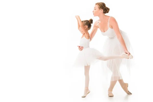 Vista lateral de la entrenadora femenina adulta en tutú ayudando a la pequeña bailarina a ejercitarse aislada sobre fondo blanco - foto de stock