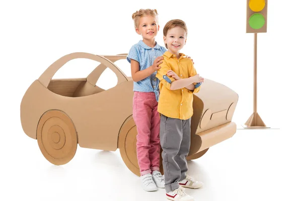 Щасливі діти позують біля картонного автомобіля і світлофорів, на білому — стокове фото