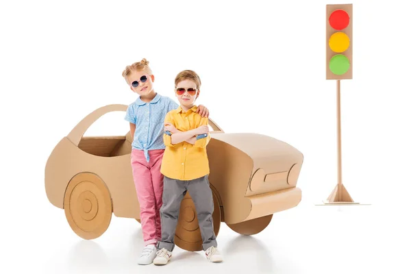 Stylish kids in sunglasses posing near cardboard car and traffic lights, on white — Stock Photo