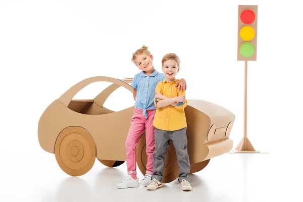 Adorable smiling kids posing near cardboard car and traffic lights, on white — Stock Photo