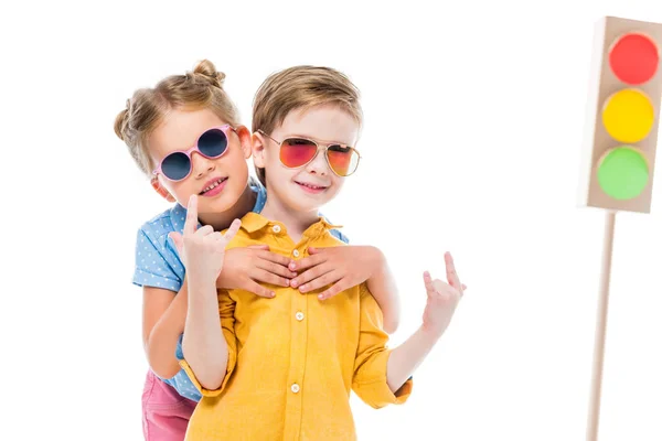 Stylish children in sunglasses, boy showing rock n roll signs, isolated on white with cardboard traffic lights on background — Stock Photo