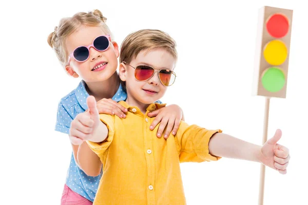 Niños con estilo en gafas de sol, niño mostrando pulgares hacia arriba, aislado en blanco con semáforos de cartón en el fondo - foto de stock