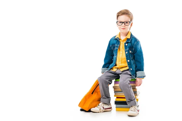 Colegial sentado en un montón de libros con mochila, aislado en blanco - foto de stock