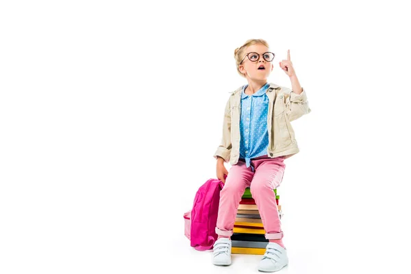 Excité écolier pointant vers le haut et ayant l'idée tout en étant assis sur une pile de livres avec sac à dos isolé sur blanc, étudiant concept — Photo de stock