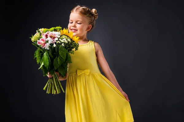 Enfant gai en robe jaune tenant bouquet de fleurs, isolé sur gris — Photo de stock