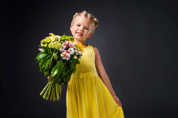 Adorable stylish kid in yellow dress holding bouquet, isolated on grey — Stock Photo