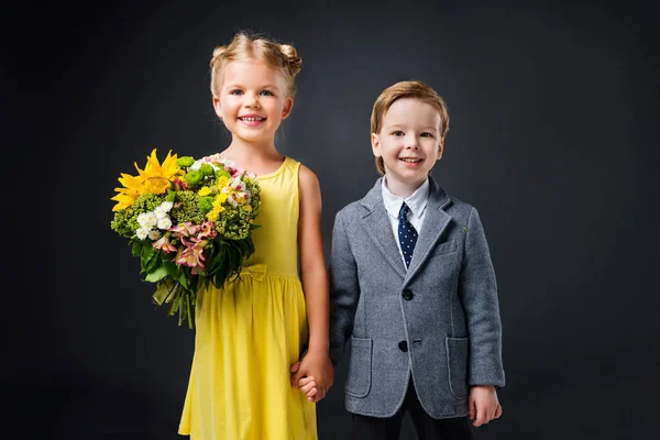 Ragazzo che si tiene per mano con bambina con mazzo di fiori, isolato su grigio — Foto stock