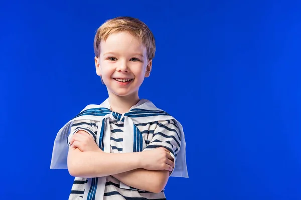 Lächelnder Junge posiert in gestreiftem T-Shirt mit verschränkten Armen, isoliert auf blau — Stockfoto