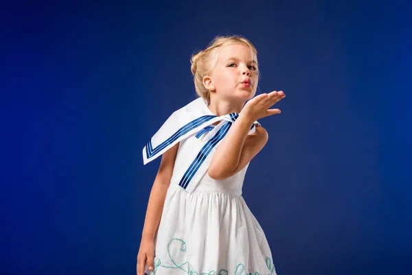 Adorable blonde child in sailor costume blowing kiss, isolated on blue — Stock Photo