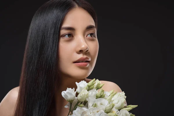 Portrait of asian woman with beautiful dark hair and bouquet of white eustoma flowers isolated on black — Stock Photo