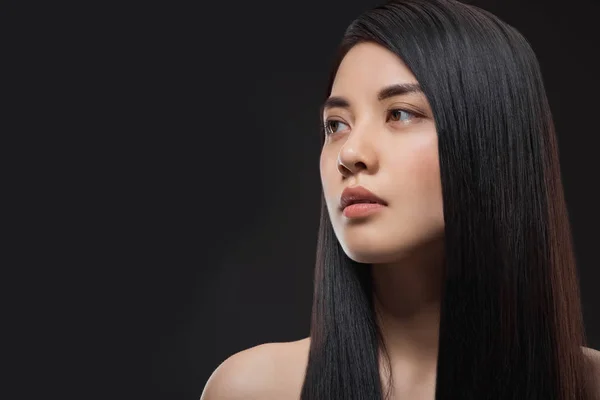 Portrait of pensive asian woman with healthy and strong hair isolated on black — Stock Photo