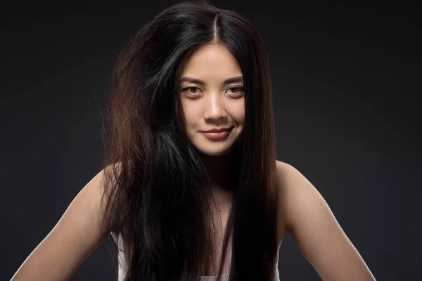 Retrato de mujer asiática sonriente con pelo medio anudado y liso aislado en negro, queratina concepto de tratamiento capilar - foto de stock