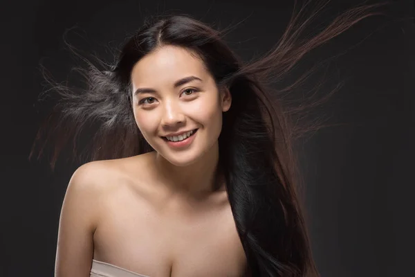 Retrato de mujer asiática sonriente con cabello sano y fuerte aislado en negro - foto de stock
