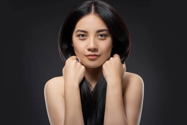 Портрет красивой азиатской женщины со здоровыми и сильными волосами, смотрящей в камеру, изолированную на черном — стоковое фото