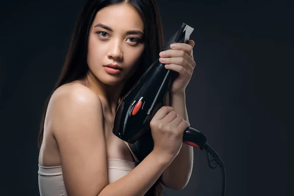 Portrait of asian woman with hair dryer looking at camera isolated on black — Stock Photo