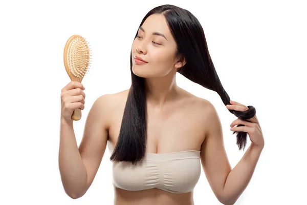 Portrait of beautiful asian woman looking at hair brush in hand isolated on white — Stock Photo