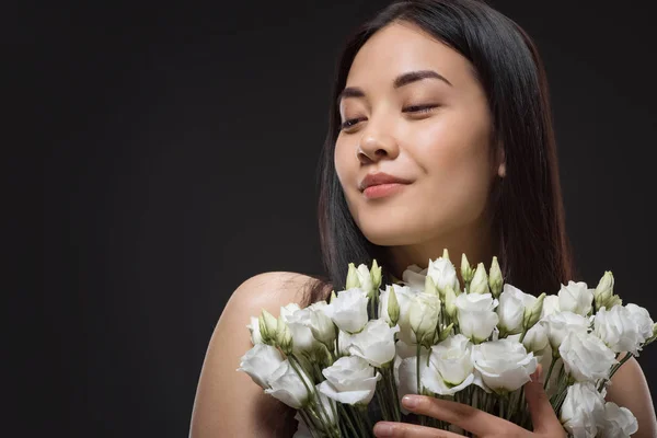 Portrait of asian woman with beautiful dark hair and bouquet of white eustoma flowers isolated on black — Stock Photo