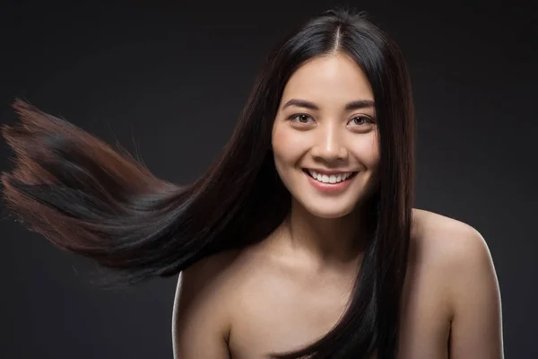 Retrato de sonriente mujer asiática con hermoso y saludable cabello oscuro mirando a la cámara aislada en negro - foto de stock