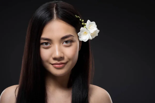 Retrato de hermosa sonriente mujer asiática con flores blancas en el pelo aislado en negro - foto de stock