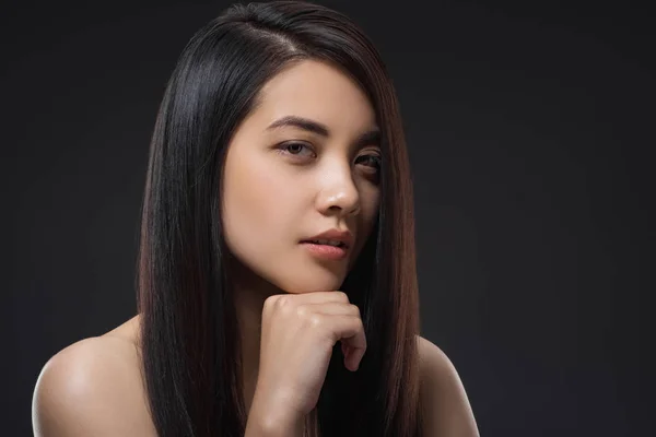 Retrato de joven mujer asiática con hermoso y saludable cabello oscuro mirando a la cámara aislada en negro - foto de stock