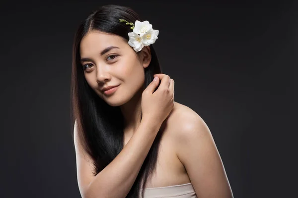 Retrato de hermosa joven mujer asiática con flores blancas en el pelo aislado en negro - foto de stock