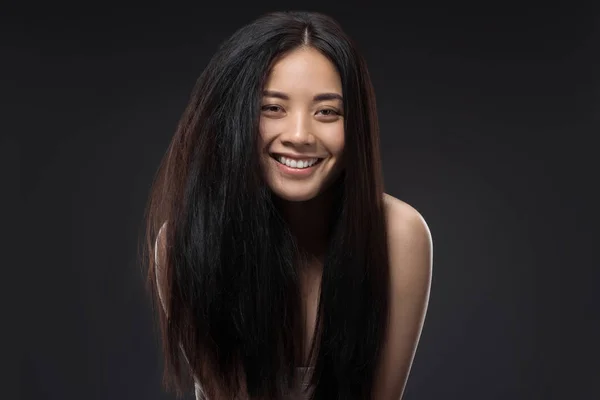 Retrato de mujer asiática feliz con hermoso y saludable cabello oscuro mirando a la cámara aislada en negro - foto de stock