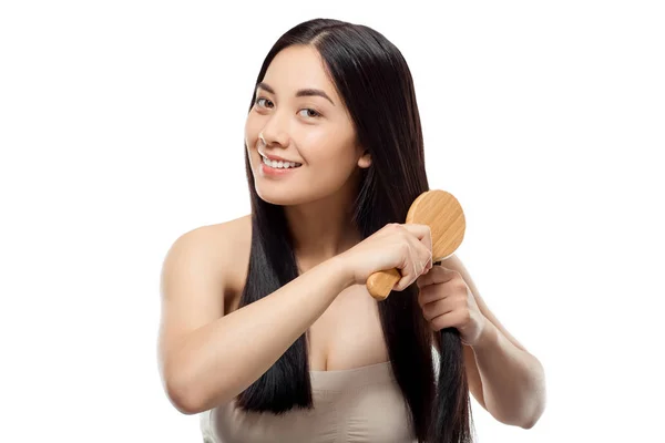 Portrait of smiling beautiful asian woman brushing hair isolated on white — Stock Photo