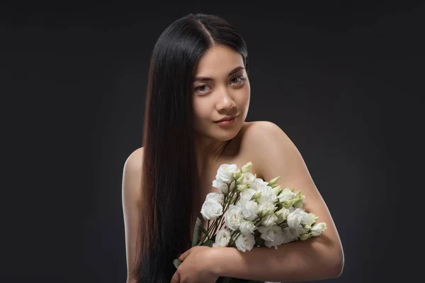 Portrait of asian woman with beautiful dark hair and bouquet of white eustoma flowers isolated on black — Stock Photo