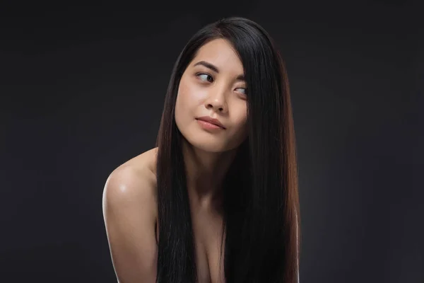 Retrato de joven mujer asiática con hermoso y saludable cabello oscuro mirando hacia otro lado aislado en negro - foto de stock