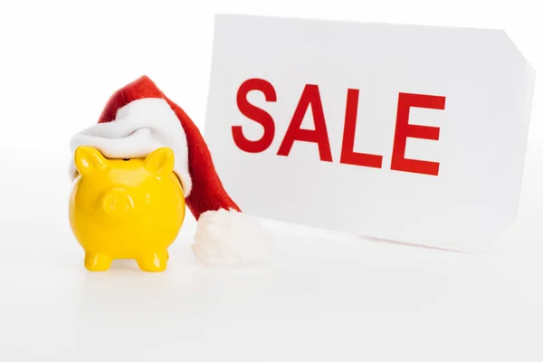 Yellow piggy bank in santa hat and sale sign isolated on white — Stock Photo