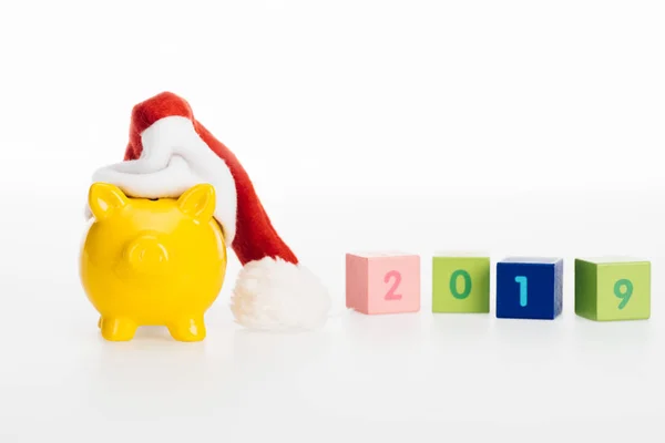 Vue rapprochée du symbole 2019 sur cubes, tirelire jaune et chapeau de Père Noël isolés sur blanc — Photo de stock